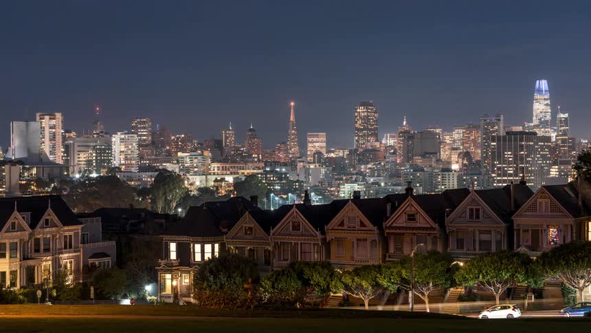 A row of victorian style houses known as the painted ladies is captured in the foreground with the san francisco skyline visible in the distance