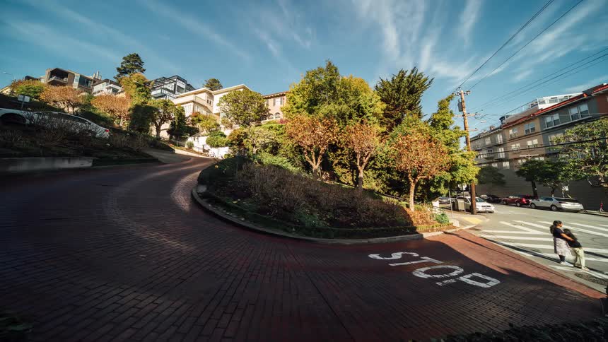 Lombard street in san francisco showcasing its curves surrounding houses trees and occasional car traffic under a bright partly cloudy sky