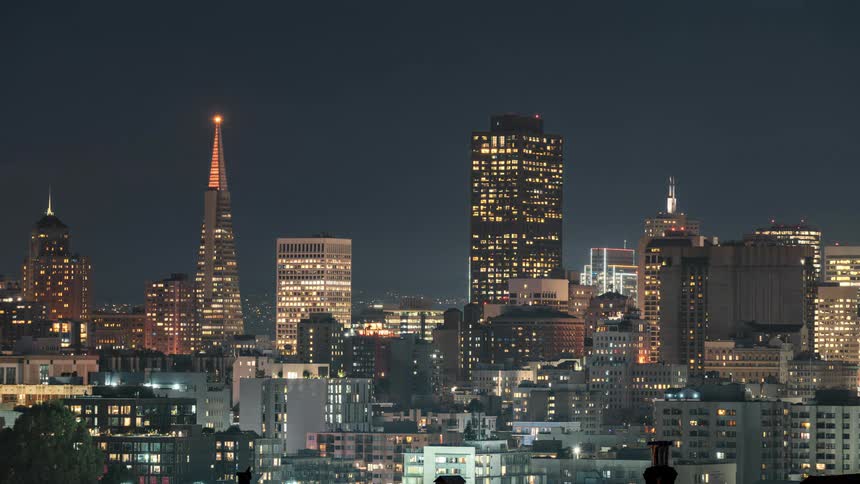 A cityscape with illuminated buildings against a dark sky showcasing a skyline with various architectural styles