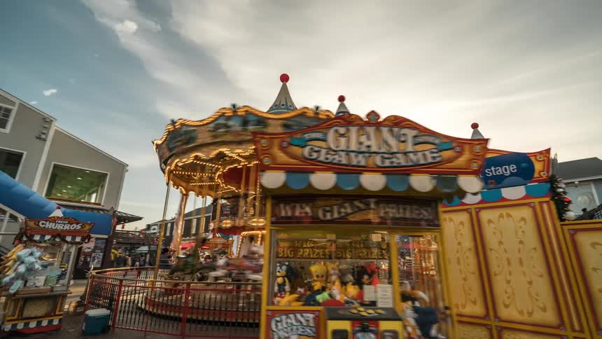 Amusement park attendees walk through the area around a busy merry go round on a cloudy day