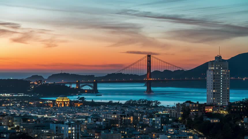 A cityscape view of the golden gate bridge and a tall building against a sunset sky