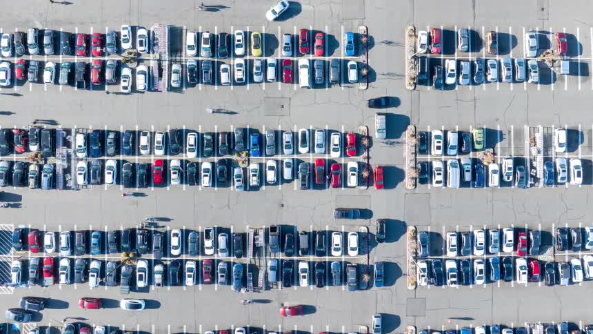 Ascending top down hyperlapse of a large parking lot with numerous vehicles and people moving in all directions