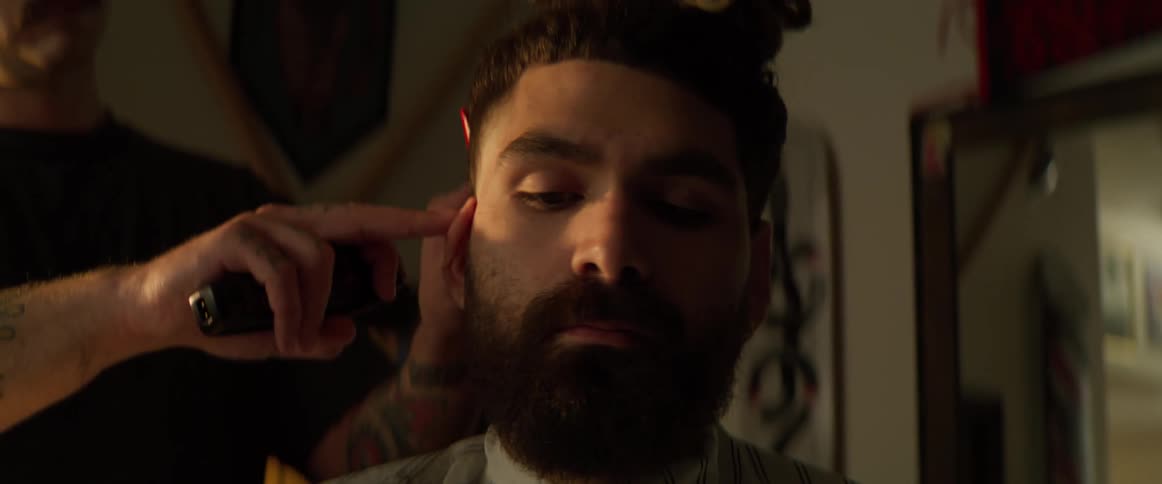 A barber is trimming a mans hair as he sits