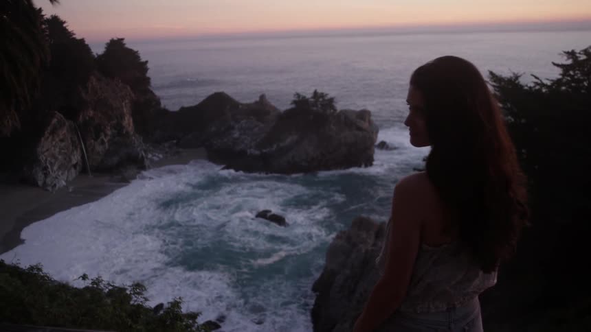 A woman standing near the edge of a cliff with water underneath