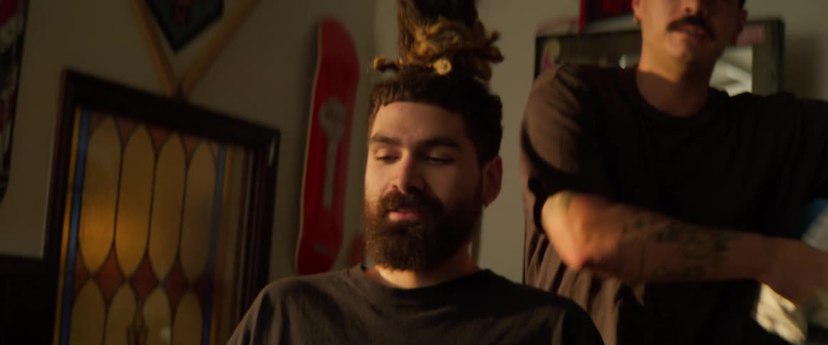 Guys greeting each other and then one sits down to get a haircut or a shave