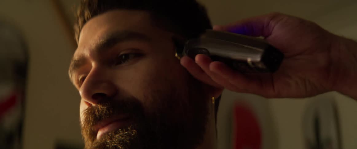 A man sits as a barber uses clippers to trim his hair