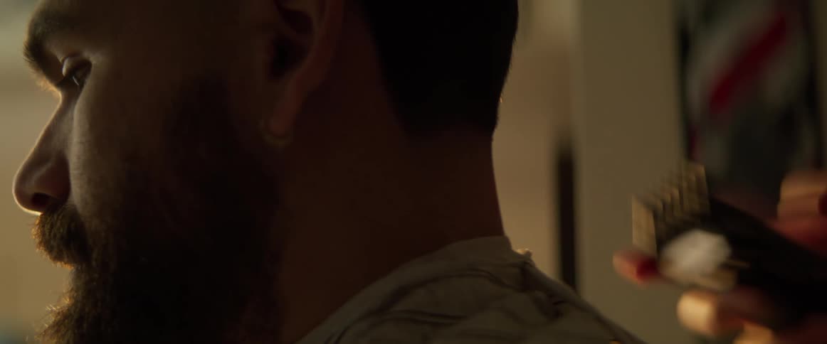A barber is trimming a bearded mans neck hairs using a hair clipper