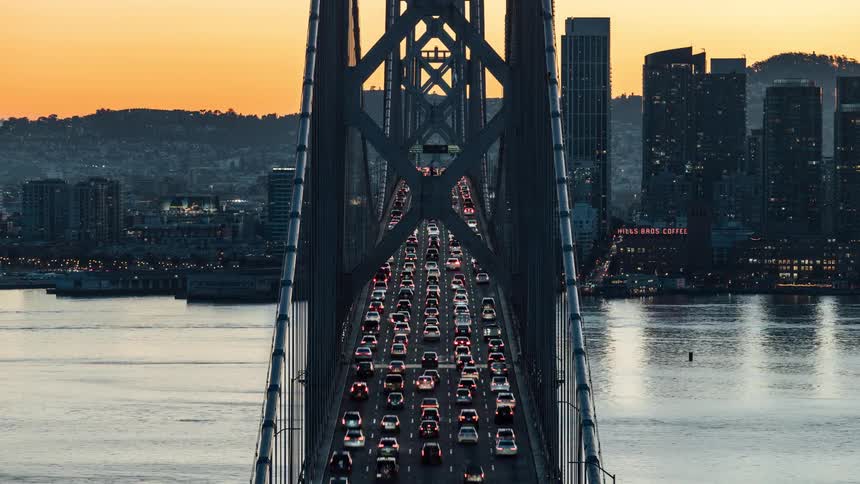 Boats pass under a busy bridge leading to downtown as day becomes night