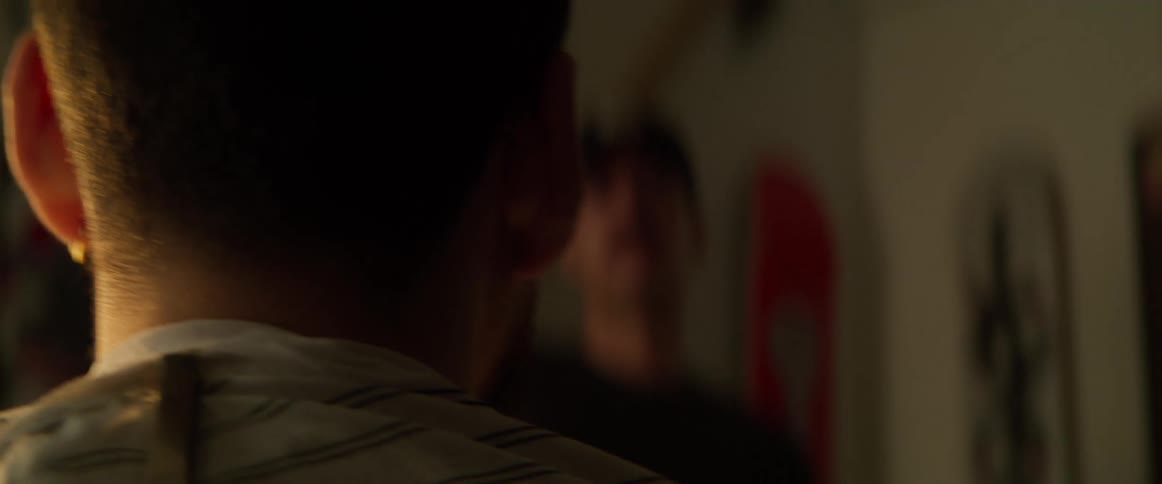 A closeup of a persons neck with a barber cape as a barber trims their hair in a dimly lit room