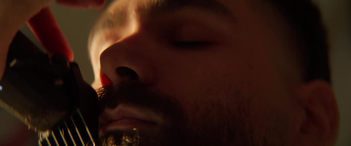 A man is trimming a customers beard with a razor