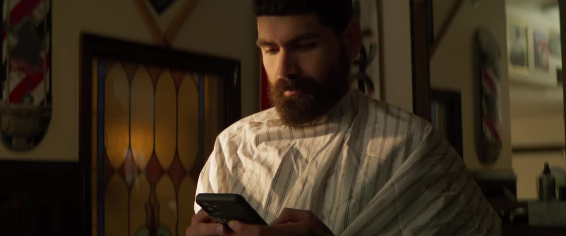 Man in a barber cape looks at his phone