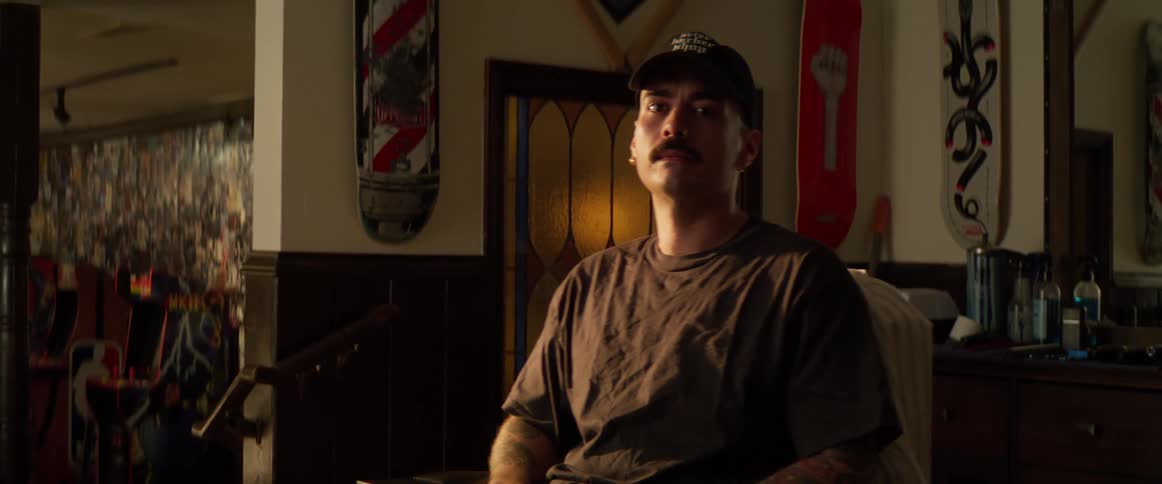 A man sitting down puts a hat on and looks into the camera