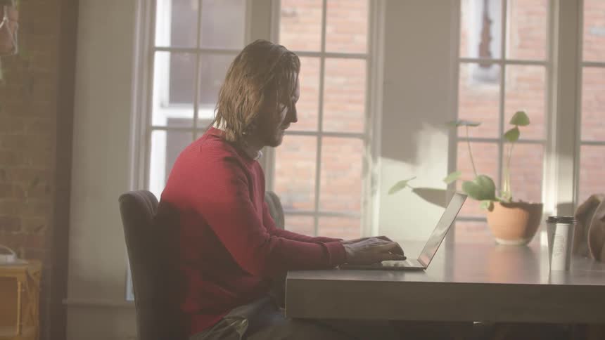 Man sitting at a table typing on a laptop computer