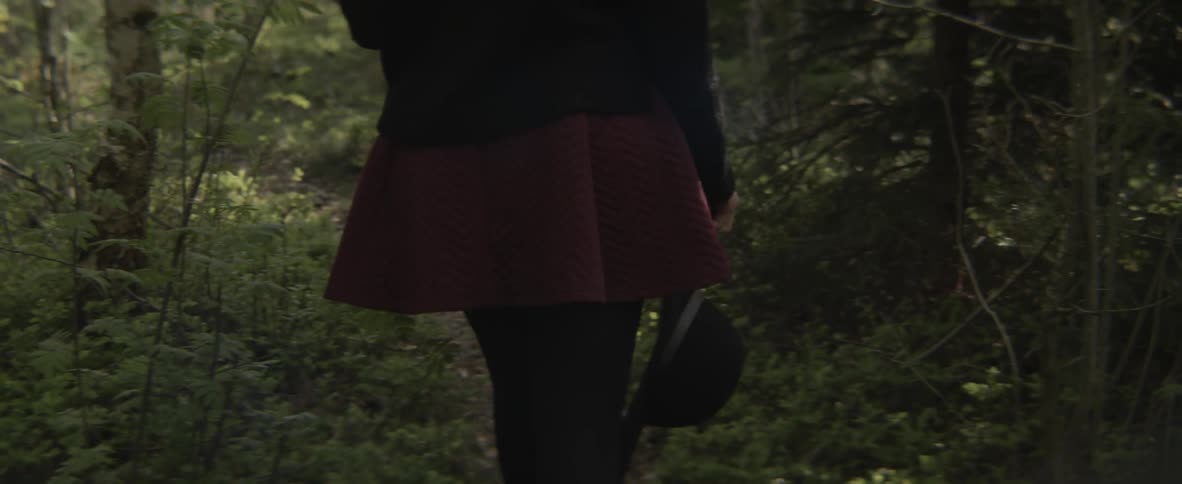 A woman carrying a hat is walking on a path in a wooded area