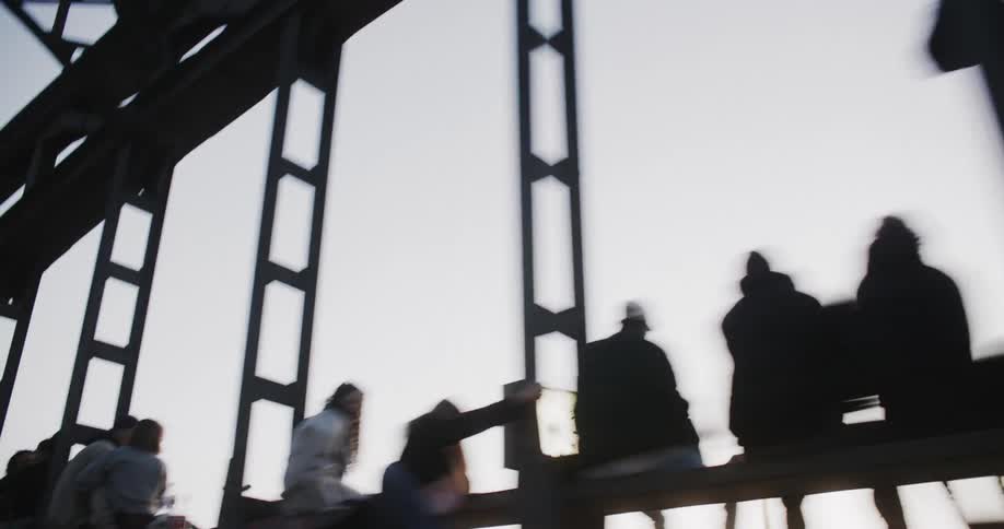 A large group of people are sitting by the railing of the bridge