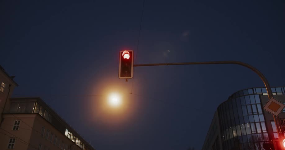 A traffic light glows against a dark blue twilight sky with the moon shining brightly in the background