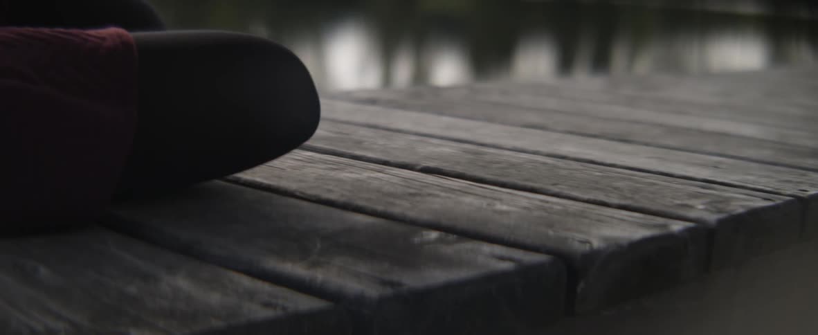 A person sitting on a dock picks up their hat