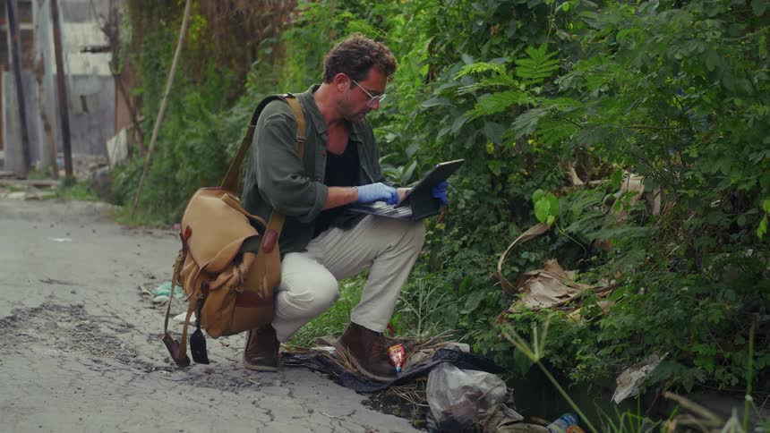 A man is typing on his tablet by the bush