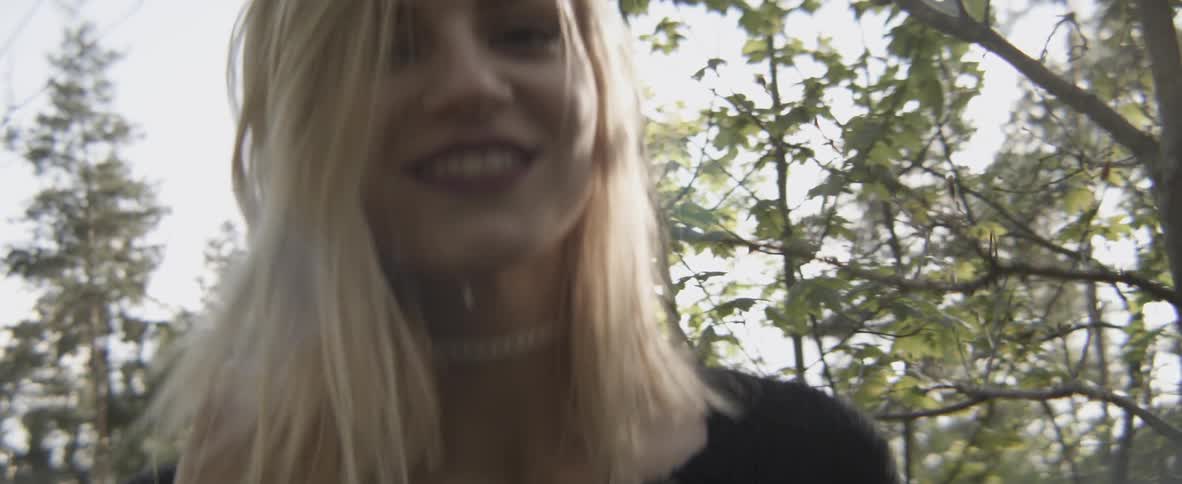 A woman pushes her hair back while smiling in a forested area