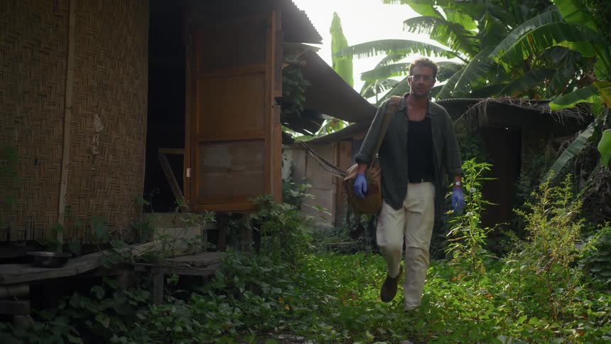 A man walks by a hut in the jungle
