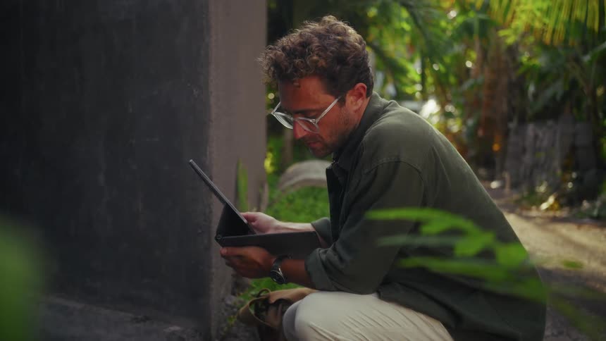 A man is looking at his tablet by the jungle