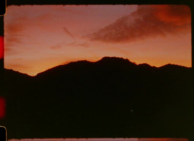 A dusky sunset with silhouetted mountains against a warm orange tinted sky