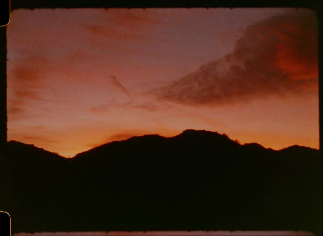 A sunset with a dark silhouette of mountains against a vibrant orange and red sky