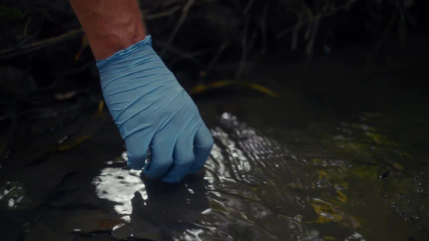 A man fills a small jar with water from the stream