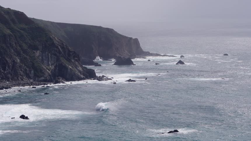 Waves roll into shore and splash against rocks along the coast