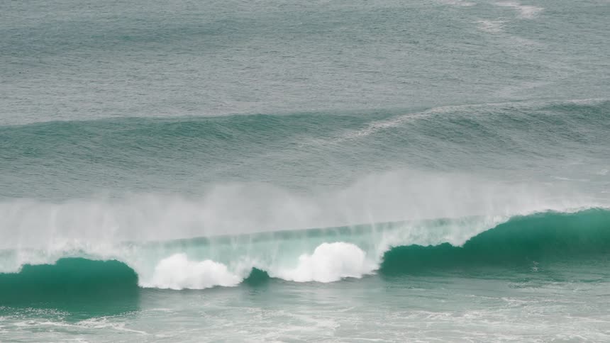 A large wave with white foam crests and breaks in the ocean