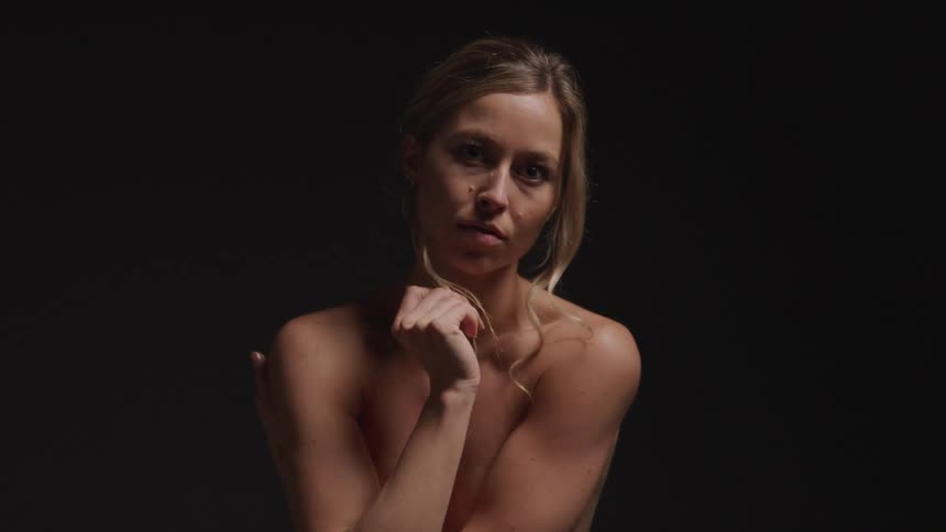 A woman in a dimly lit setting her body partially illuminated as she embraces herself with a contemplative expression evoking a sense of vulnerability and introspection