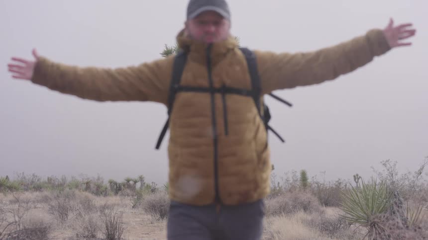 Man backpacking through the desert enjoying snow flurries