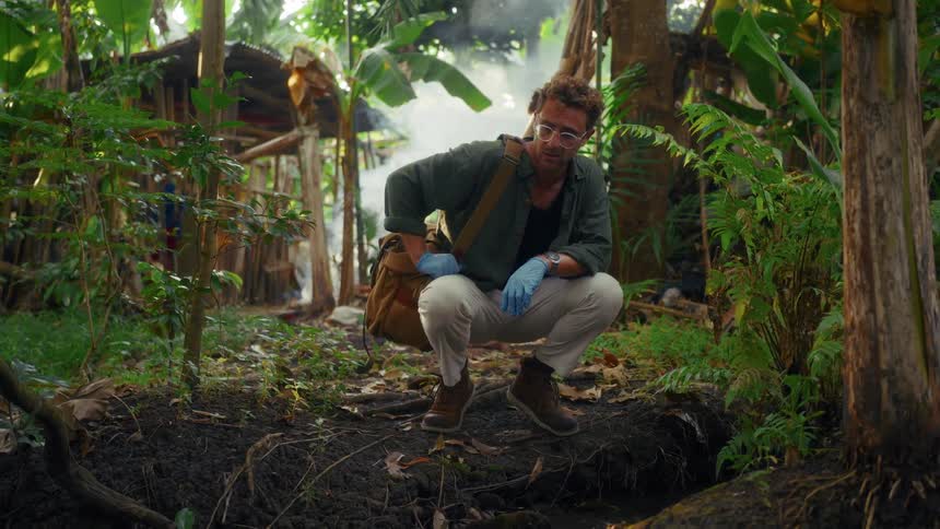 Man squats in front of a hole in the middle of the forest and rummages through his bag