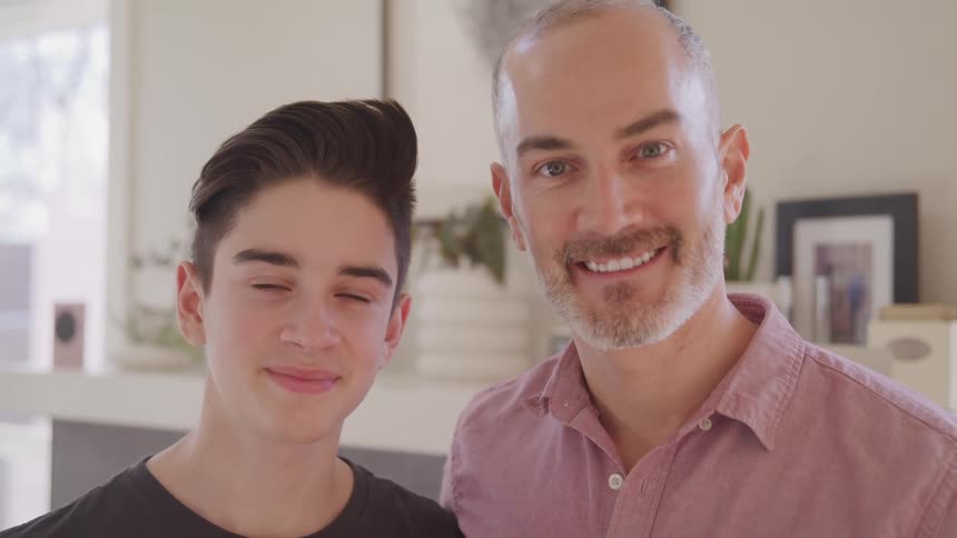 Father and son smile and stand in front of a mantel