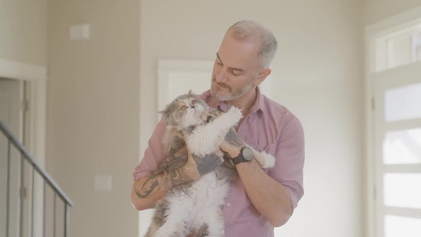 A man with gray hair and a pink shirt gently holds a fluffy cat in his arms