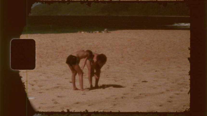 Two boys are looking down on the sand at the beach