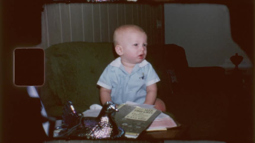 A baby boy practices standing up by holding onto a table in the living room