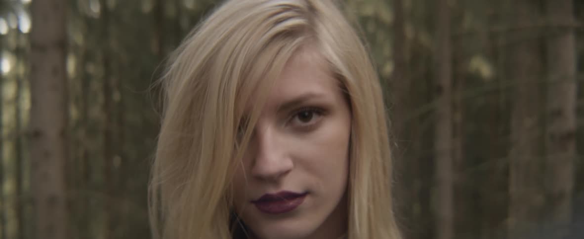A blonde woman walking outside moves her hair to the side