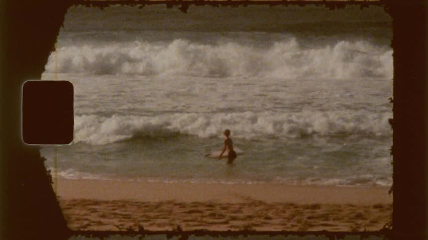A child rides a surfboard in the ocean as large waves crash behind him