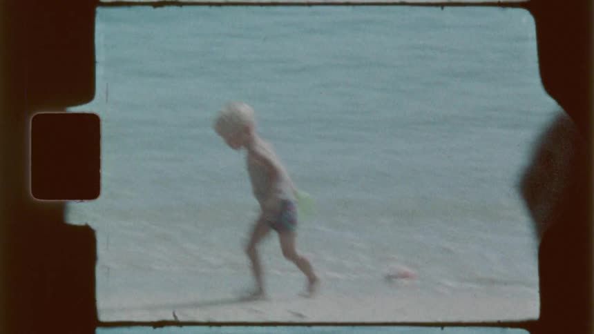 A little boy plays in the water at a beach as others watch