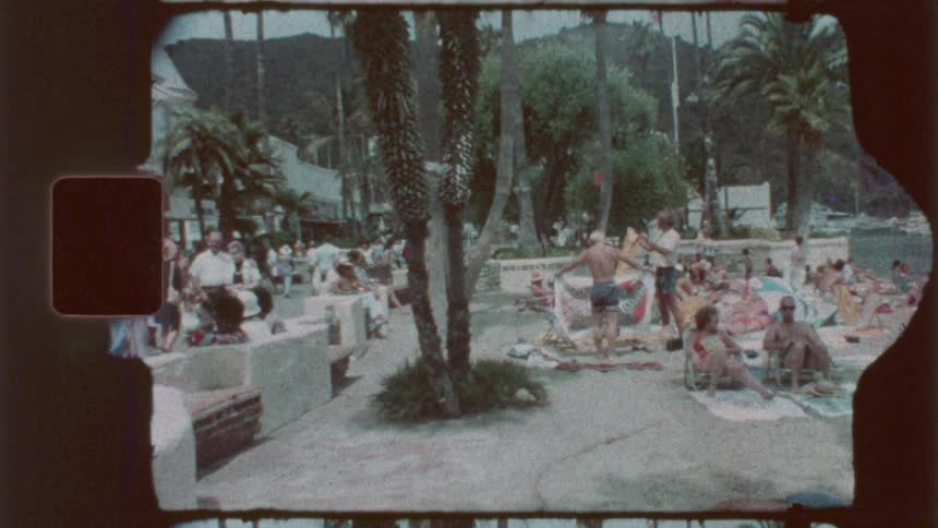 Families and friends on towels and walking around a public pool