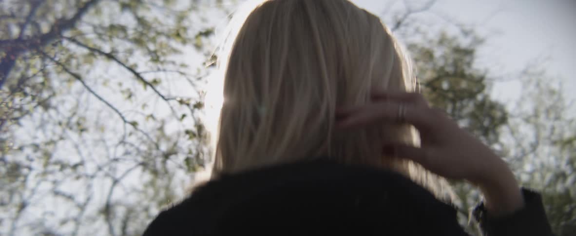 A woman is walking in the woods with the sun shining down