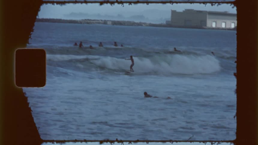 Several people surf on a slightly cloudy day with a coastal building in the background