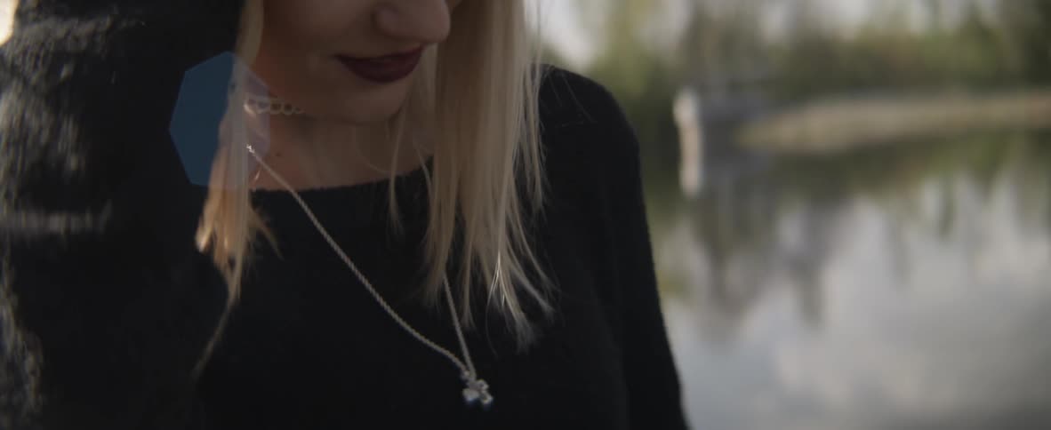 A woman touches her necklace outside near a lake