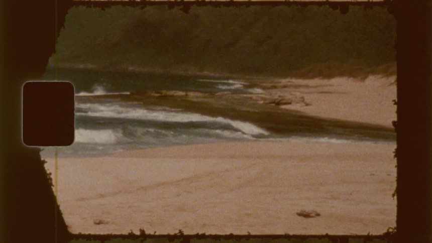 A grainy film captures a beach scene with waves meeting the shore