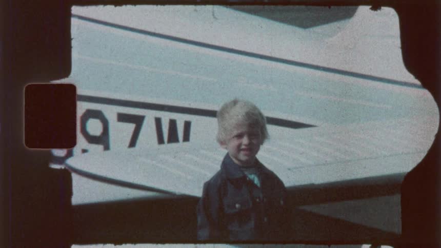 Happy young boy smiling and waving standing next to a white cessna