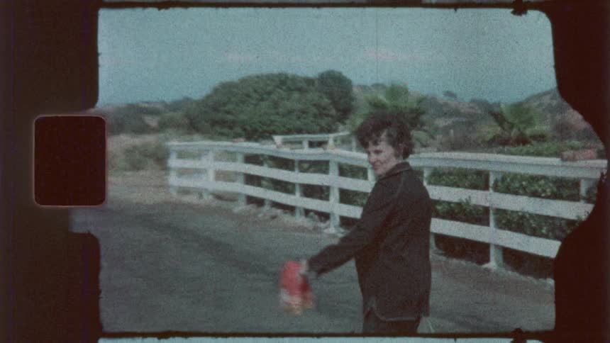 Woman walking near a white fence in the rural countryside gestures with a bag