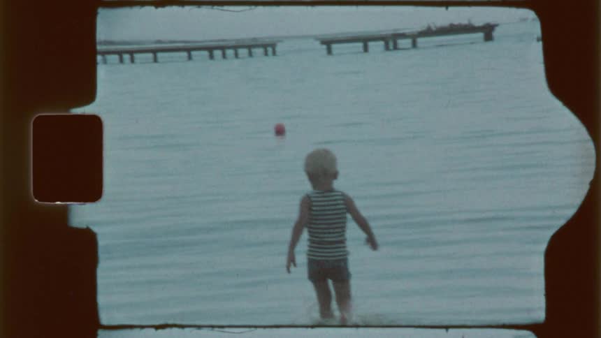 The little boy is walking out in water and he turns back and looks at whoever is filming him