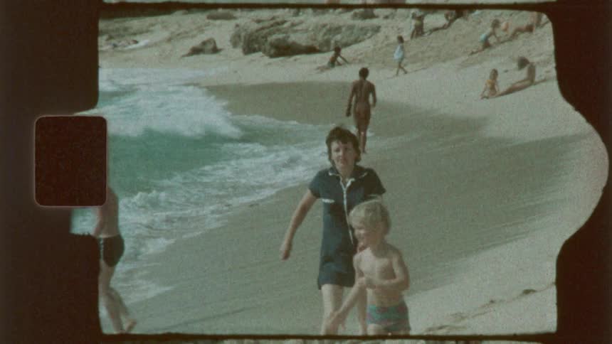 Mother and son wearing vintage swimwear walk on a sandy beach near the shoreline
