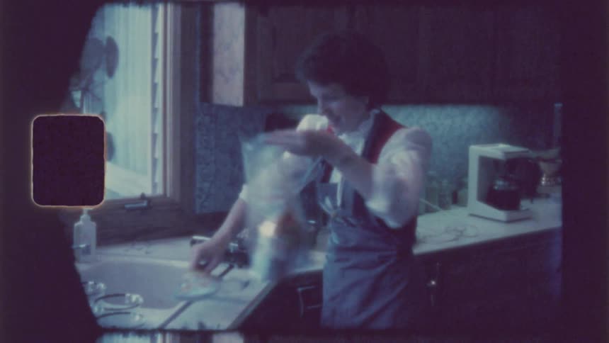 A woman smiles and waves as she cooks in the kitchen